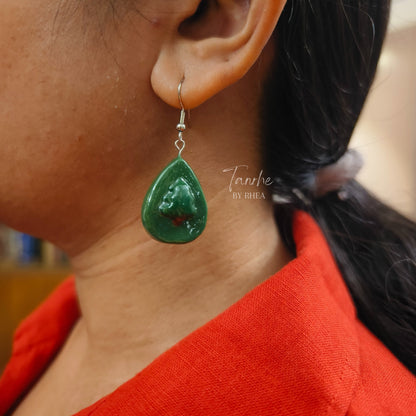Close-up of a person wearing a green christmas tree teardrop earring 
