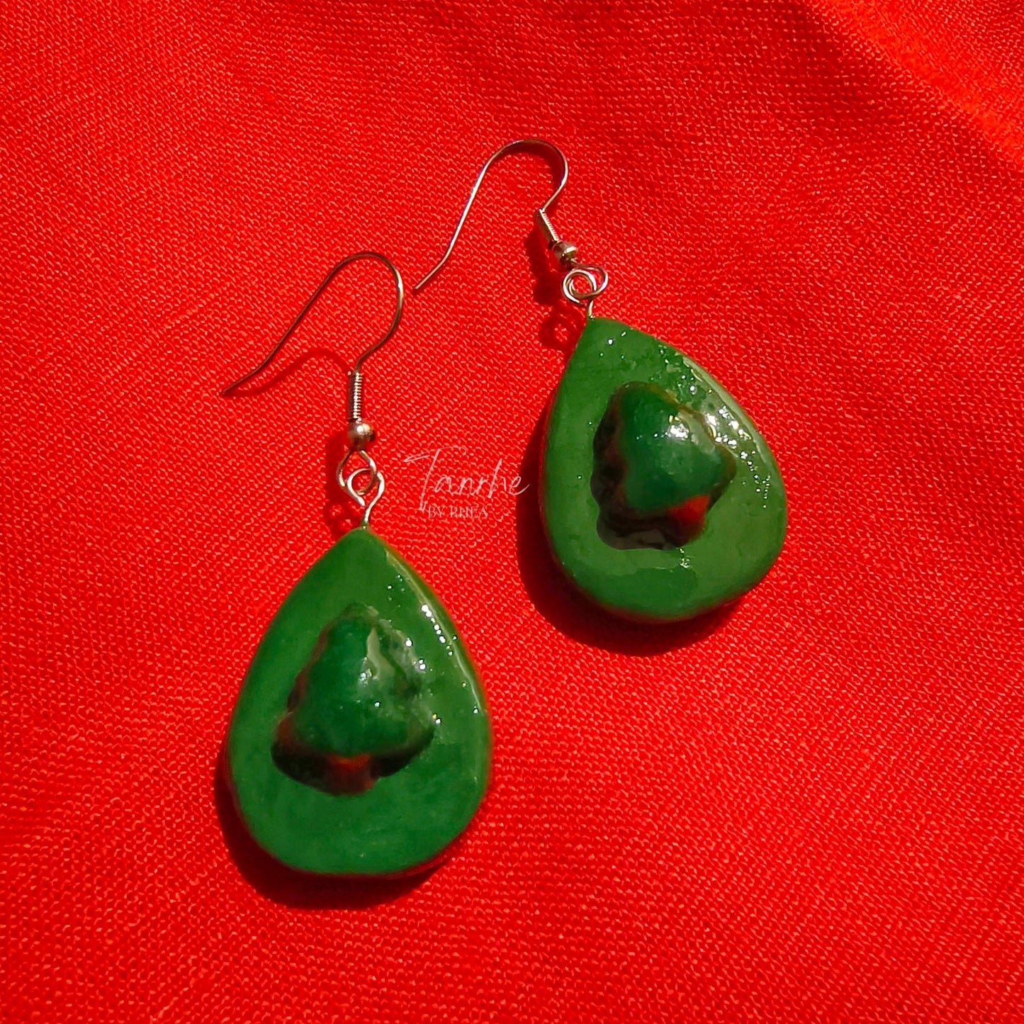 Green christmas tree teardrop earrings on a red fabric background