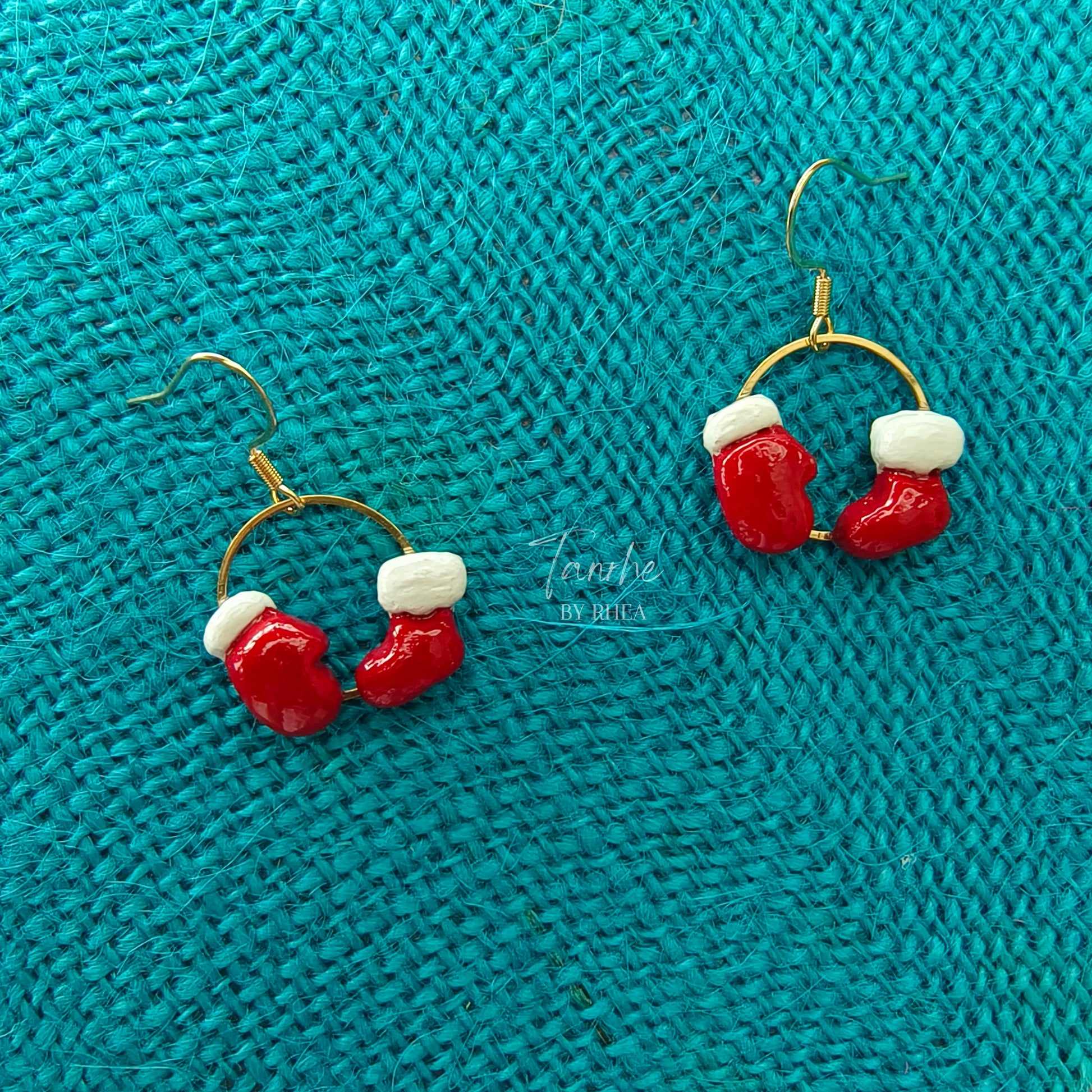 Red and white Christmas-themed sock and glove earrings on a teal textured fabric background