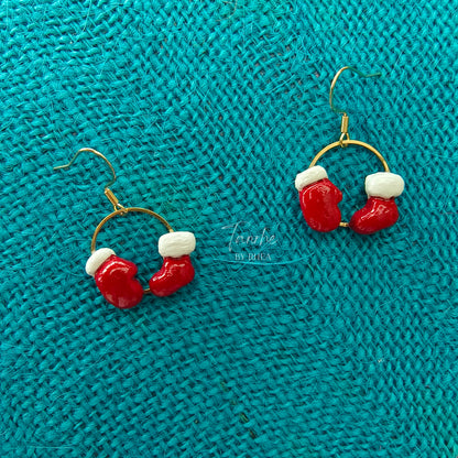 Red and white Christmas-themed sock and glove earrings on a teal textured fabric background