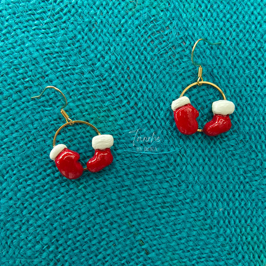 Red and white Christmas-themed sock and glove earrings on a teal textured fabric background
